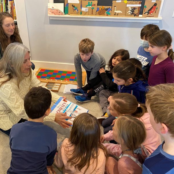 a woman shows a bundle of books and bookmarks to a group of children crowded around her.