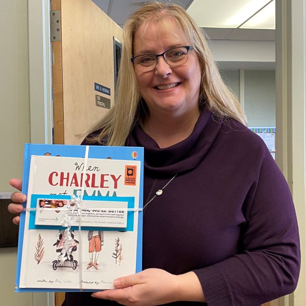 a smiling woman holds a bundle of books and bookmarks.