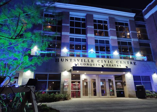 A building, the Huntsville Civic Centre, at night lit with blue and green flood lights.
