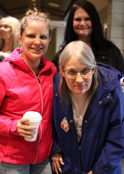 3 smiling women, 1 holding a paper coffee cup.