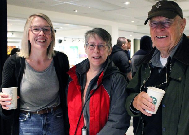 3 smiling adults, 2 holding paper coffee cups.