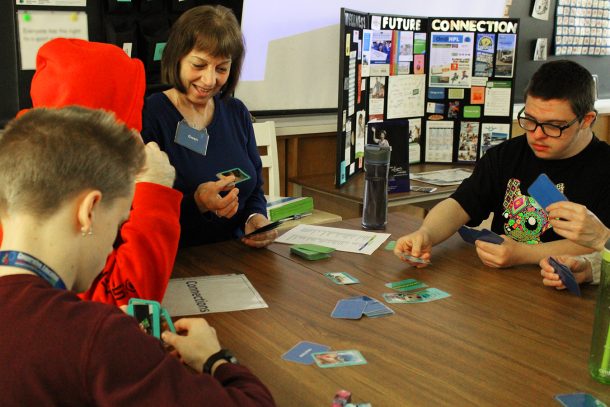 3 students and 1 adult, Gwen, sit around a table playing cards.