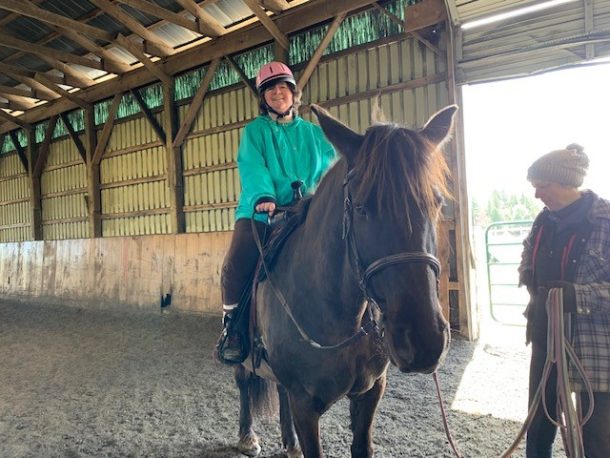 Fran with Zara A smiling woman in a green jacket and pink riding helmet on top of a dark brown horse.