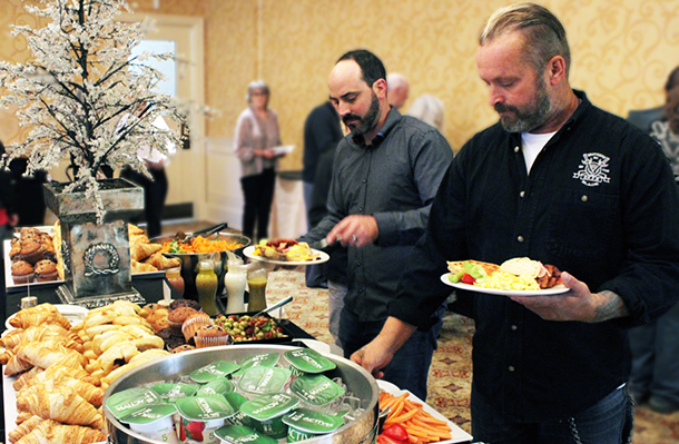 2 men holding plates choose food items from a brunch buffet.