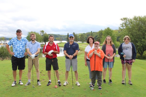 8 men and woman pose on a golf course for a group photo.