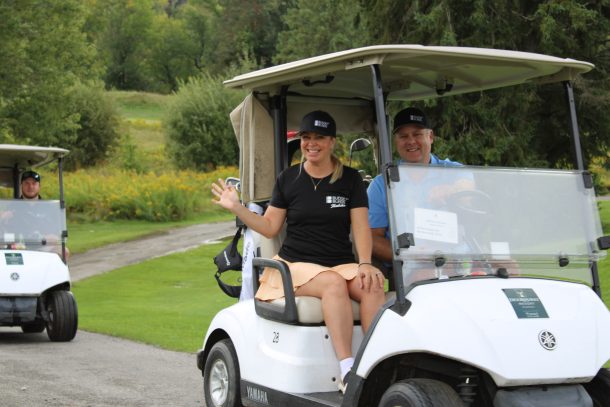 a woman and man wave from a golf cart