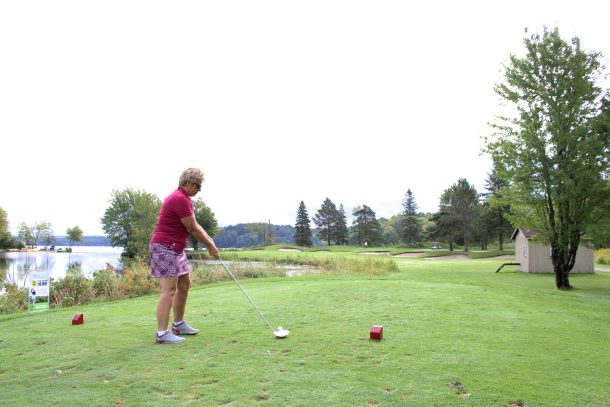 a woman tees off near a sign that reads $10,000 hole in one challenge