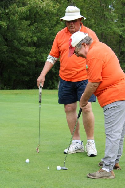 2 men sink a putt on a golf green.