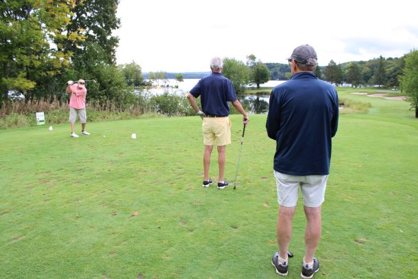 a man tees off from a golf tee while 2 teammates watch