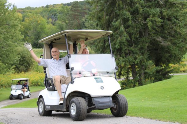 2 men wave from a golf cart