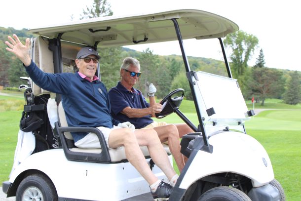 2 men wave from a golf cart