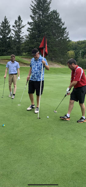 3 men putt a golf ball into the cup on a golf green