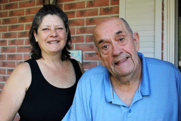 A smiling woman, Tracy, and smiling man, Jerry, on the front porch of a red-brick home.