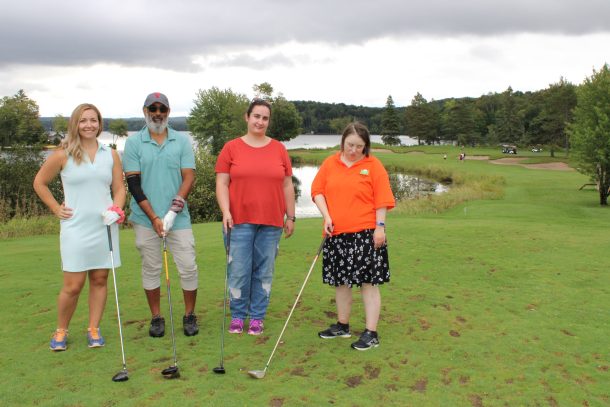 3 women and a man post for a photo at a golf tee