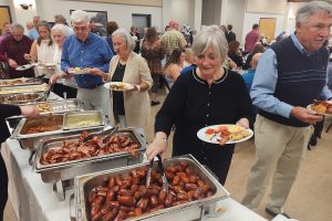 a woman using tongs to gather items from a buffet