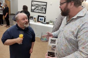 2 men in conversation, 1 holds a glass of orange juice.