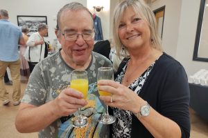 a smiling man and woman cheers with glasses of orange juice.