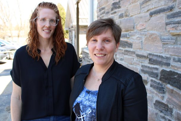 2 smiling women standing outside a stone building, which is Community Living Huntsville's administration offices.