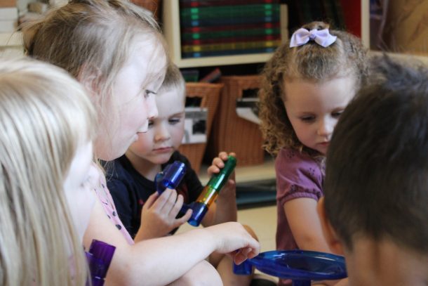 Children seated on a classroom floor sorting through a bin of toys.