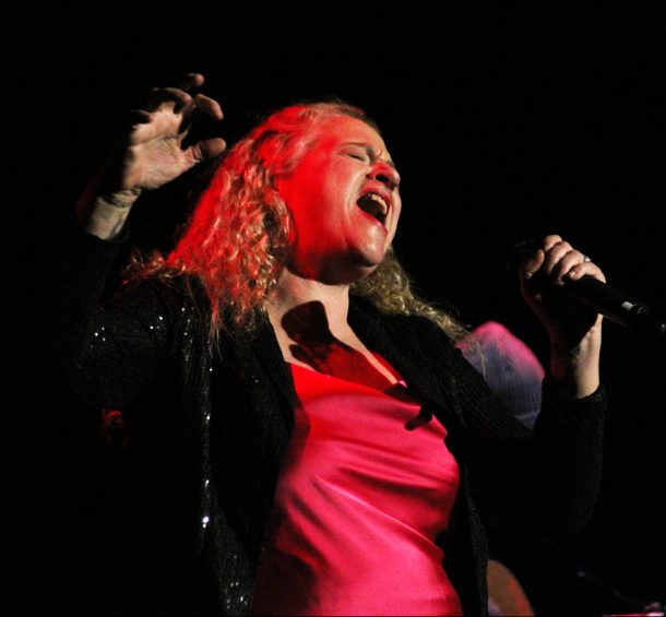 A woman in a hot pink shirt, Meredith, sings passionately into a microphone.