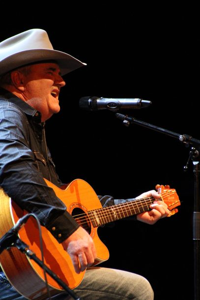 A man in a cowboy hat, Ray, sings while playing a guitar.