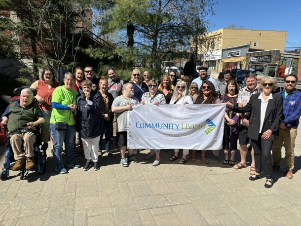 30 people gathered around a white flag that features the Community Living logo