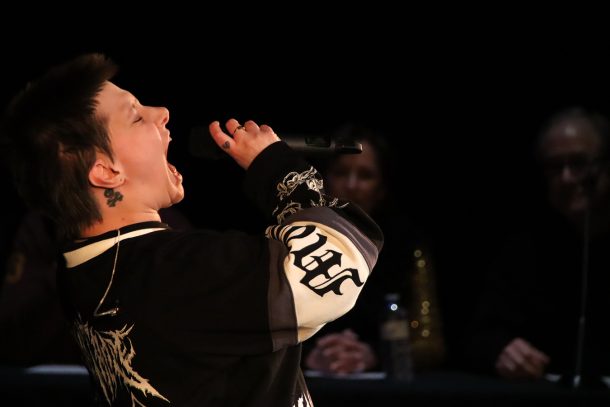 A woman in a black and white jersey leans back and screams into a microphone