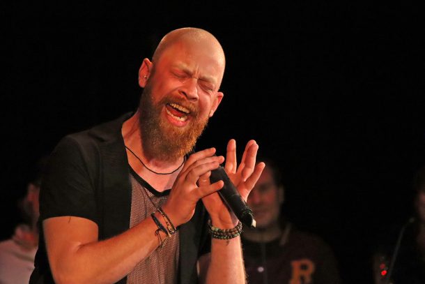 A man with a beard sings passionately into a microphone
