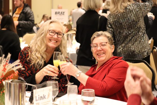 2 smiling women cheers with glasses filled with orange juice