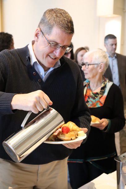 A smiling man pours syrup from a silver container onto its waffles