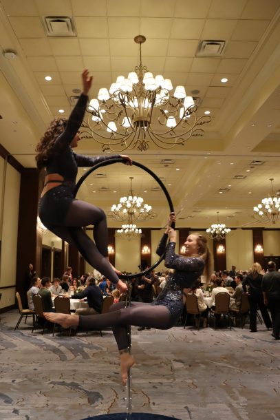 2 aerial gymnasts on a lollypop hoop in a crowded ballroom