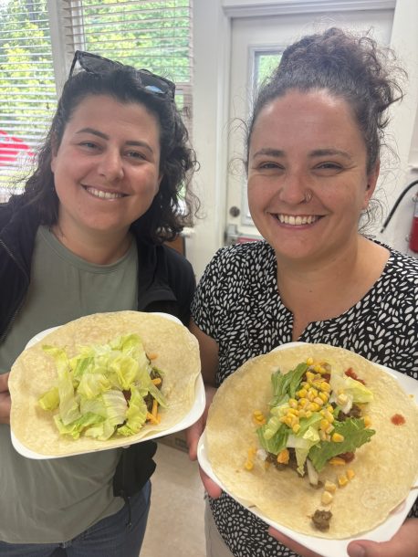 2 smiling women holding plates filled with soft flour tortilla burritos