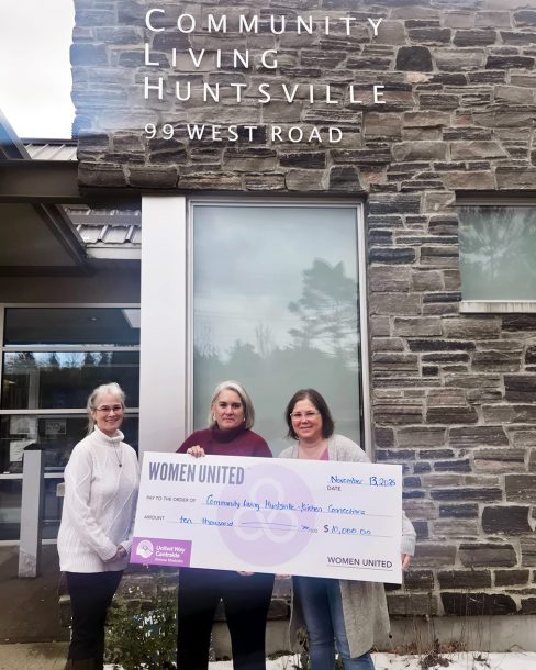 3 women outside Community Living Huntsville's administrative office hold a large novelty cheque for $10,000.
