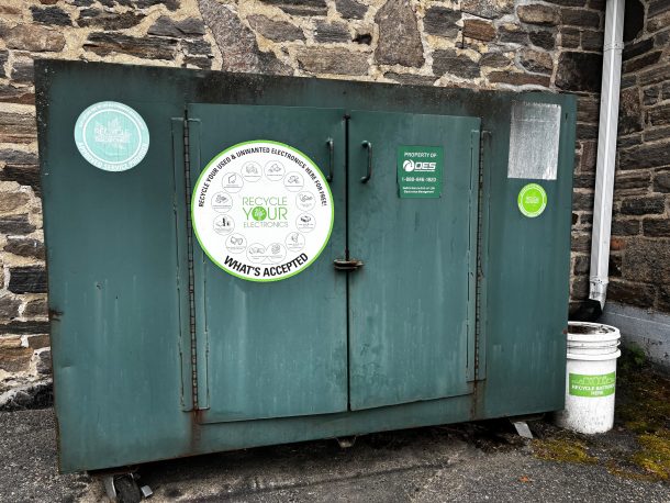A large green metal bin with 2 doors on the front and a white sticker that reads, "Recycle Your Electronics".