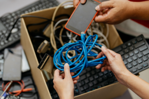 2 sets of hands sorting through a box of old household electronics.