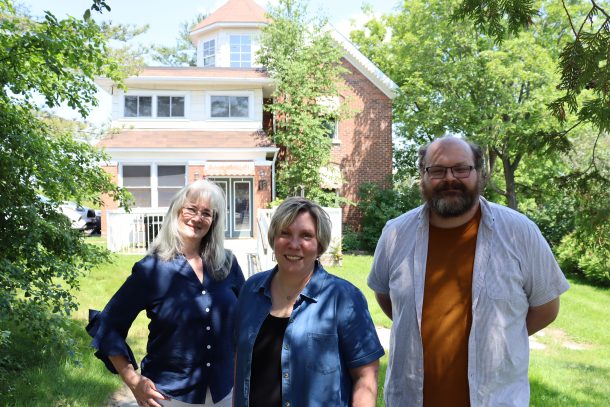3 people, Diane, Suzanne, and Chris, stand under the stand of a tree. There is a house behind them, Floral Villa.