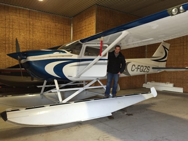 A man in an airplane hanger standing beside a float plane.