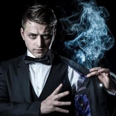 A man, Yan Markson, opens his suit jacket to reveal smoke rising from the interior pocket.