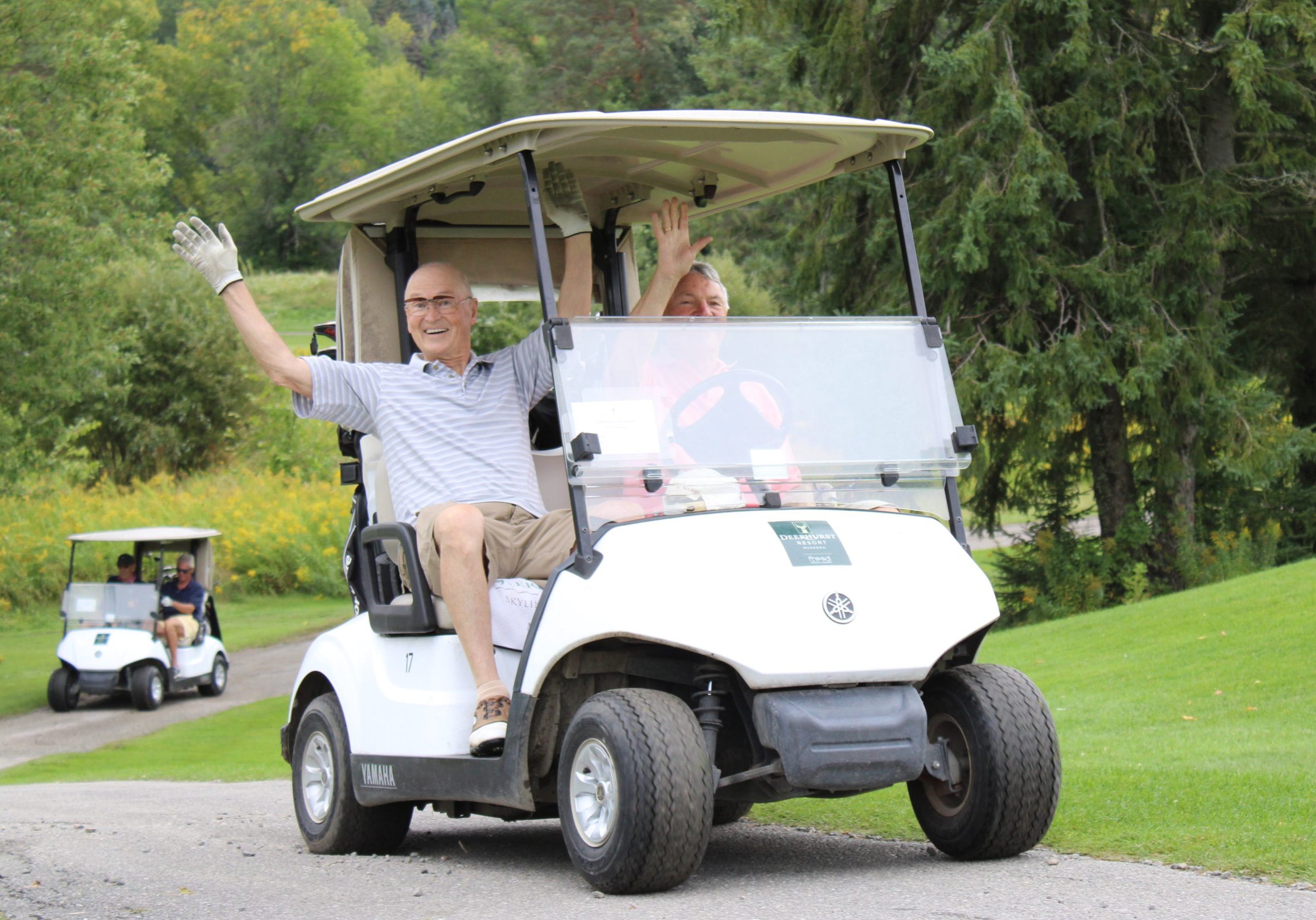 2 men in a golf cart raise their hands in the air in cheer.