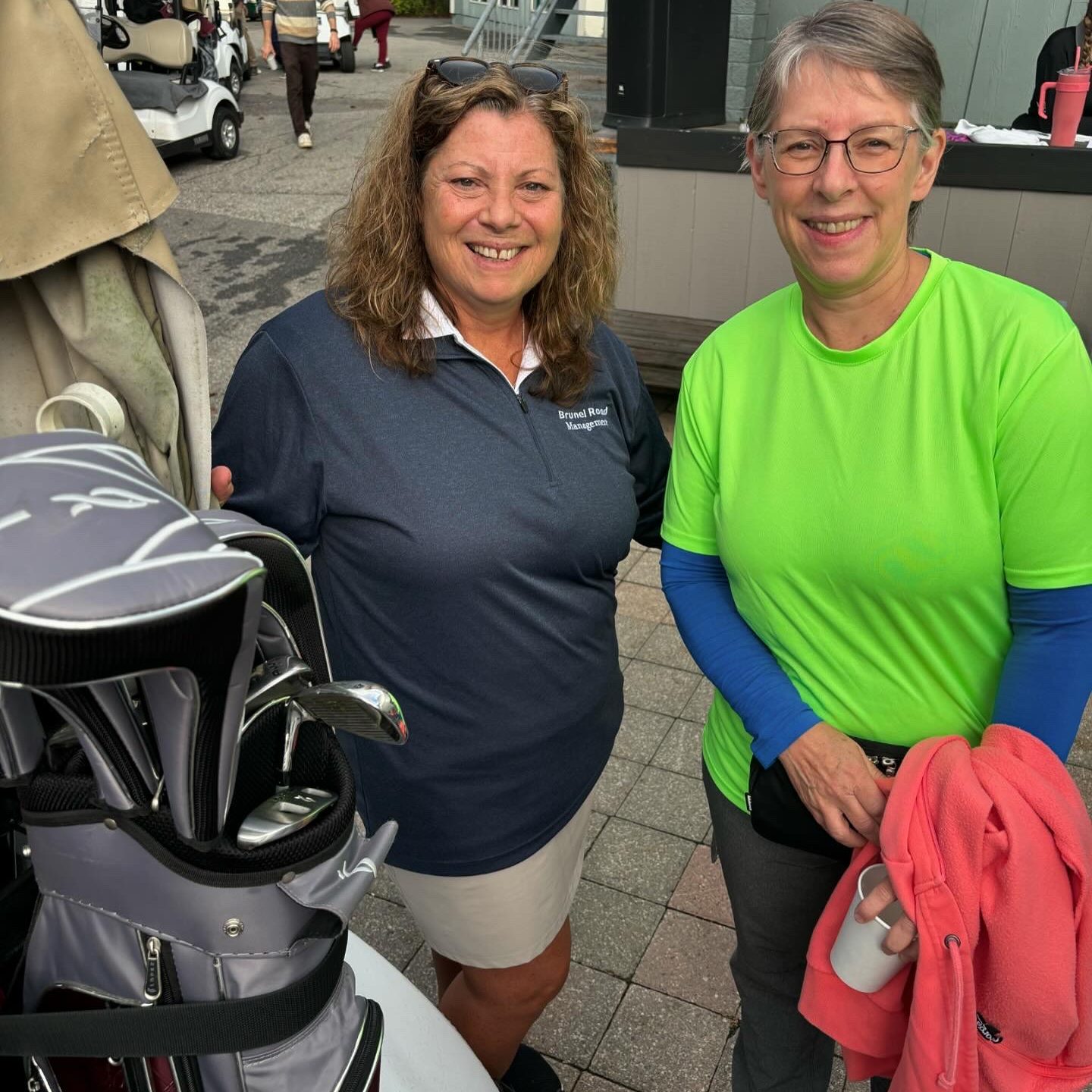2 smiling women pose for a photo beside a golf cart.