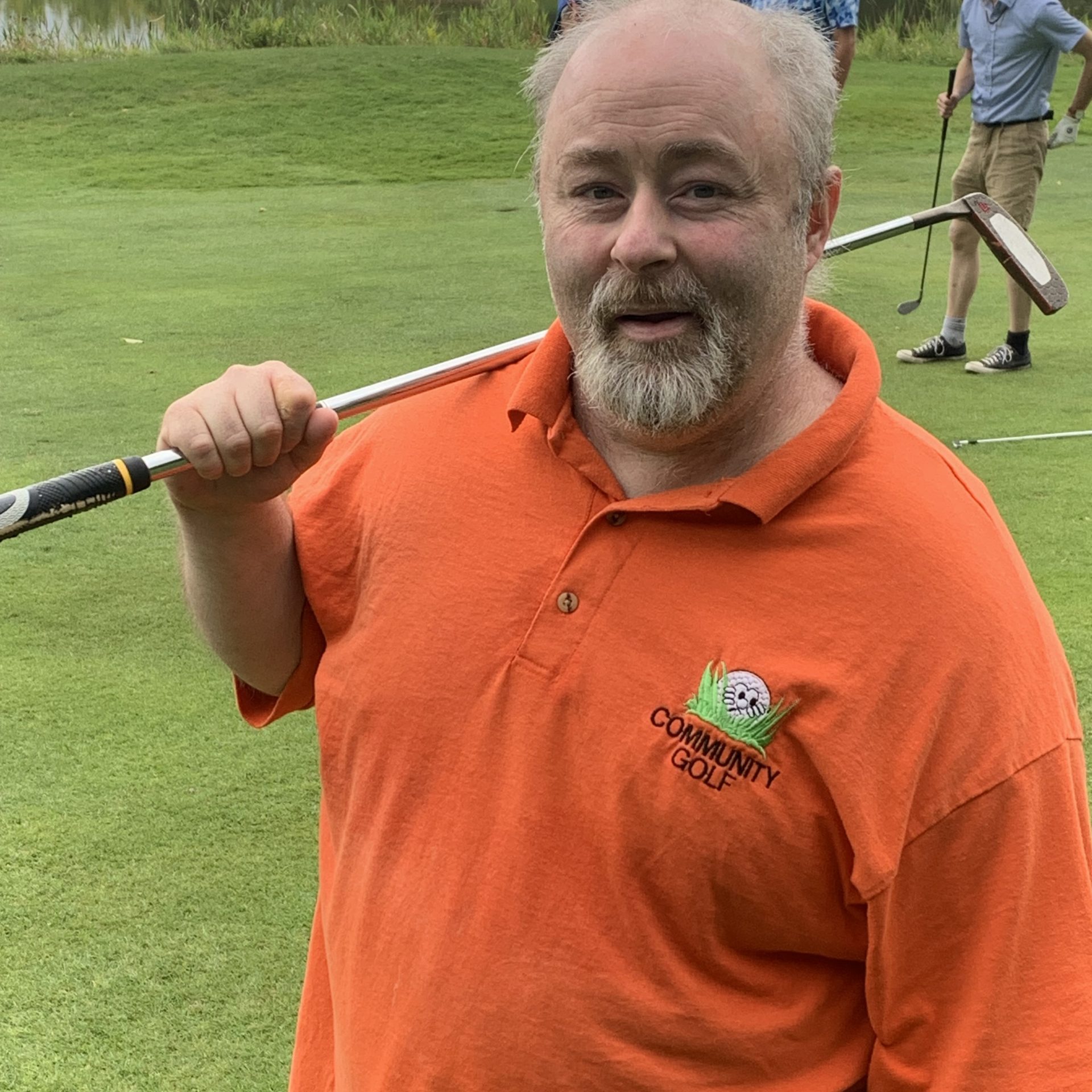 Man with grey hair and orange polo shirt rests a golf club on his shoulder